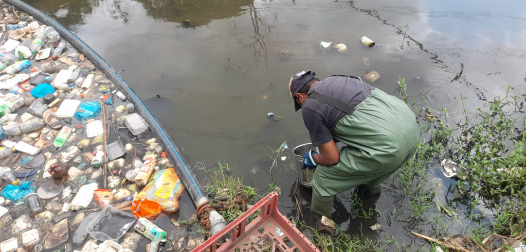 Person bending down next to river litter boom with a bucket